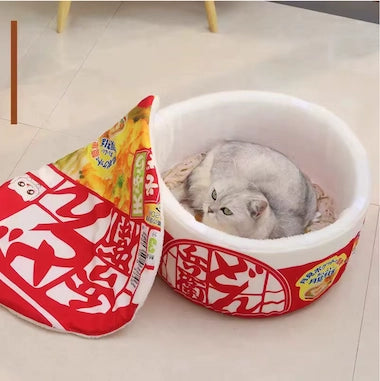 Cat lying inside a Ramen Noodle Cat Nest on a light-colored floor.